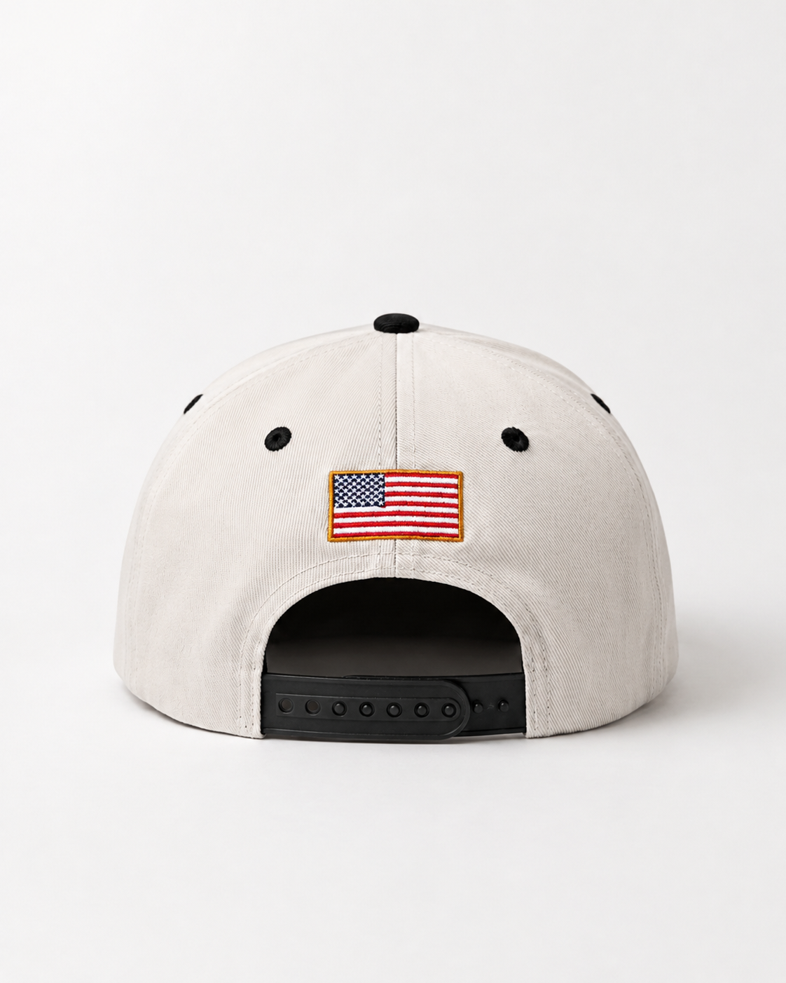 A light beige structured baseball cap shown from the back, featuring a small embroidered American flag patch centered above the black snapback closure.