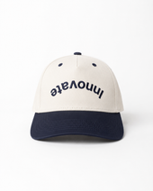 A baseball cap with an off-white crown and a navy blue brim, featuring the word 'Innovate' embroidered in navy blue on the front.