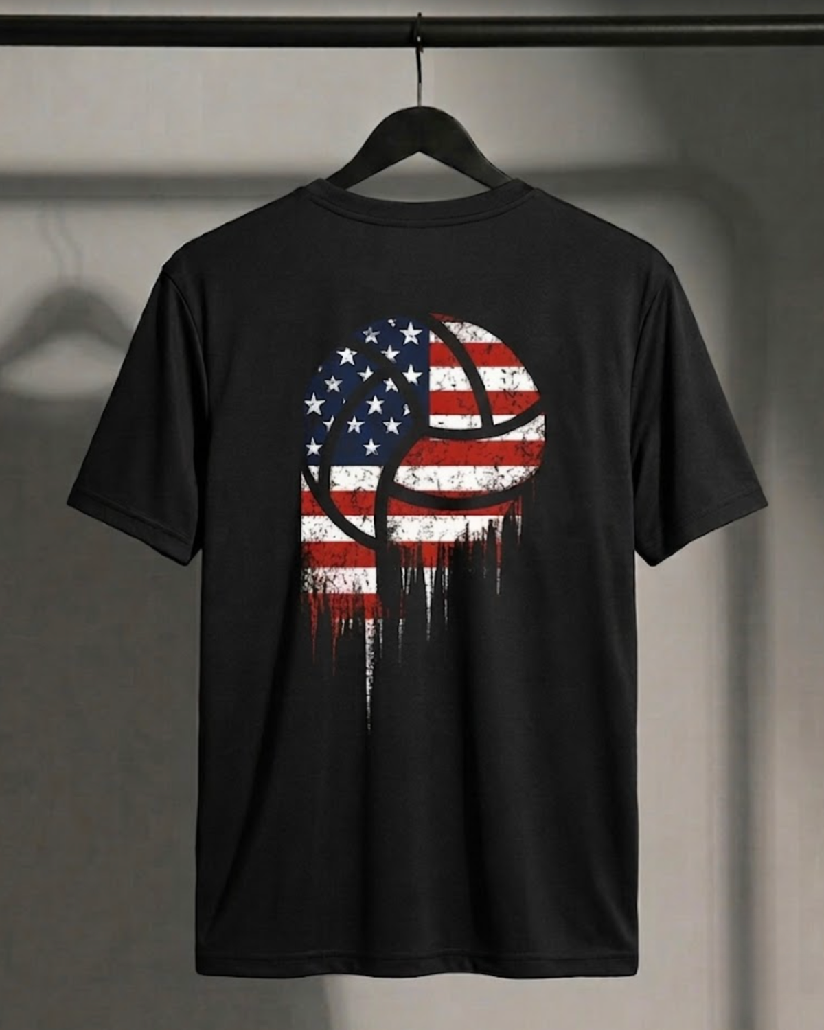 A black short-sleeve t-shirt hanging on a black hanger against a gray wall. The back of the shirt features a distressed graphic of a basketball filled with the American flag pattern, with the stars and stripes dripping down like paint.
