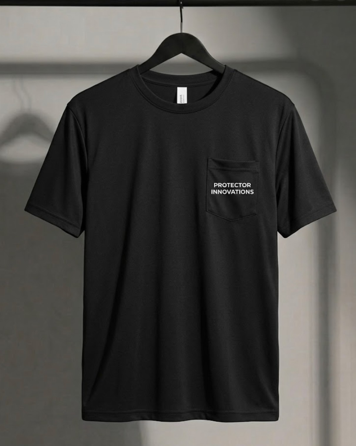 A black short-sleeve crewneck t-shirt hanging on a black hanger against a gray wall. The shirt features a left chest pocket with the text 'Protector Innovations' printed in white.