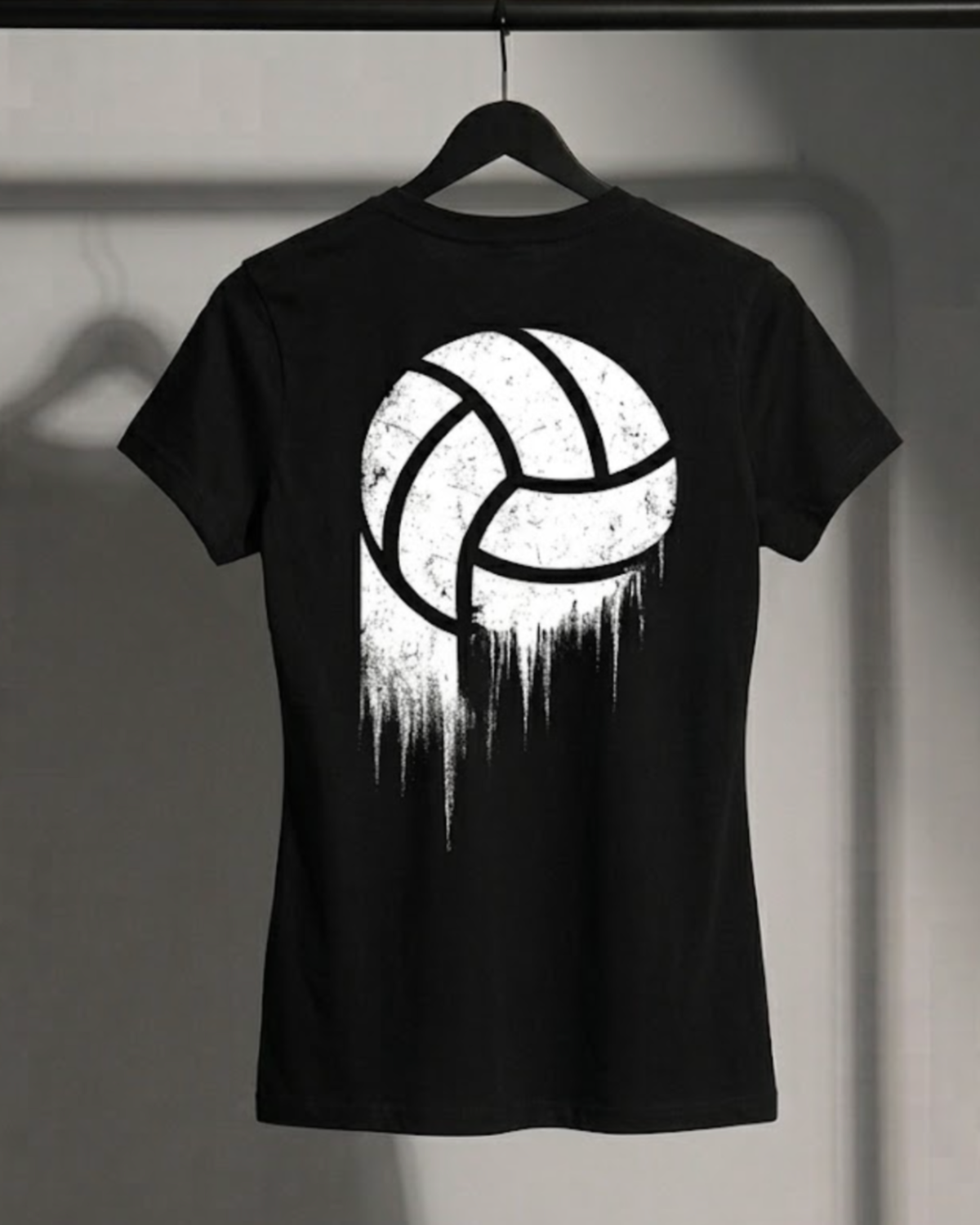 A black short-sleeve t-shirt hanging on a black hanger against a gray wall. The back of the shirt features a large white volleyball graphic with a distressed, dripping paint effect.