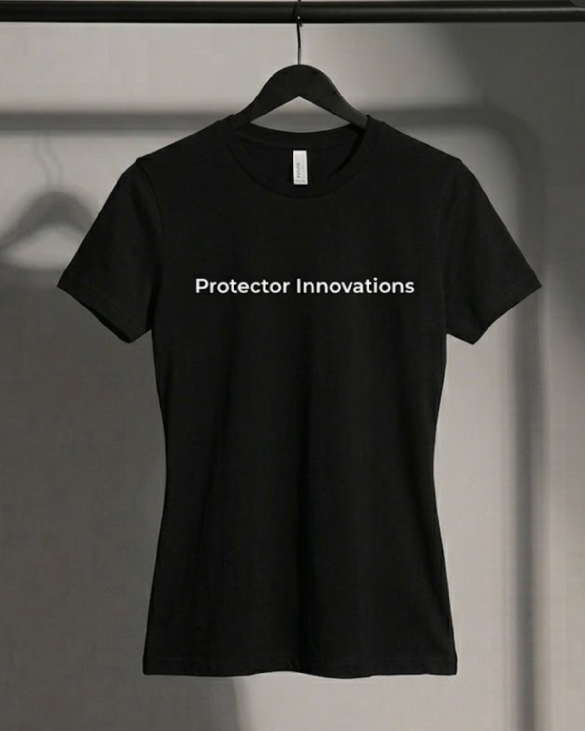 A black short-sleeve crewneck t-shirt hanging on a black hanger against a gray wall. The shirt features the text 'Protector Innovations' printed in white across the chest.