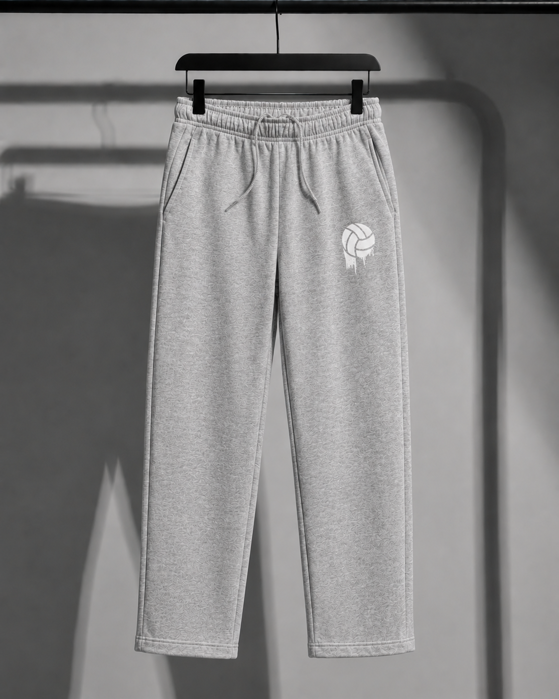 Light gray heather sweatpants hanging on a black hanger against a gray wall, featuring a white volleyball logo on the left thigh.